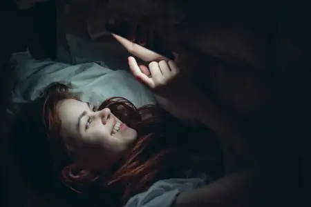 Эмоциональная женщина с телефоном в руках ночью лежит в постели