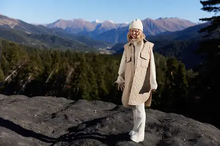 Турист в осенней одежде стоит на скале, любуясь пейзажем с голубым небом и отдыхая