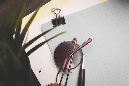 Канцелярские принадлежности: блокноты, очки, бумага со скрепкой, чашка кофе и цветок