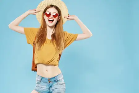 Весёлая симпатичная женщина в шляпе и солнцезащитных очках, с распущенными волосами и рюкзаком, излучает эмоции и демонстрирует определённый образ жизни