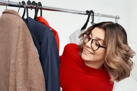 Симпатичная женщина в очках стоит рядом с одеждой, мода, веселье, изолированный фон