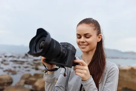 Счастливая женщина-фотограф наслаждается временем у моря, запечатлевая воспоминания с помощью цифровой камеры