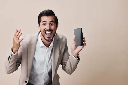 Успешный мужчина в деловом костюме держит смартфон, счастливо улыбаясь и делая селфи в студийной обстановке