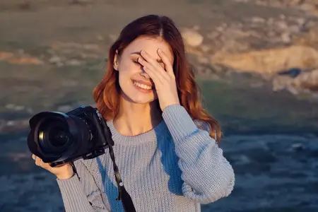 Жизнерадостная женщина-фотограф с камерой в руках на природе, в солнечный день