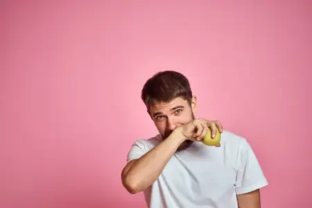 Милый мужчина с яблоком на розовом фоне жестикулирует руками, обрезанный вид, белая футболка, свободное пространство