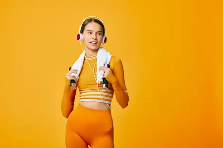 Спортивная женщина в ярком оранжевом фитнес-комплекте выполняет упражнения с гантелями, в гарнитуре, с приготовленным полотенцем, динамичная фитнес-сцена, подчеркивающая здоровье, тренировки…