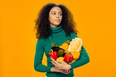 Красивая женщина в зеленой куртке держит овощи и фрукты, символизируя здоровое вегетарианское питание
