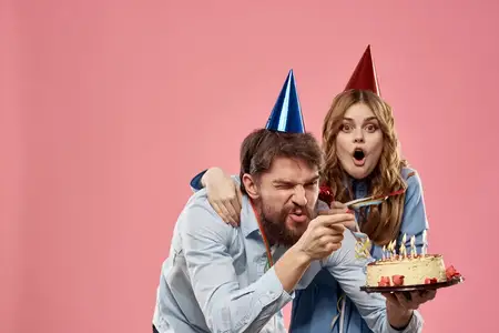 Мужчина и женщина на корпоративной вечеринке на розовом фоне веселятся с тортом и колпаком