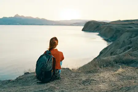 Женщина-туристка сидит на земле в горах у моря на закате