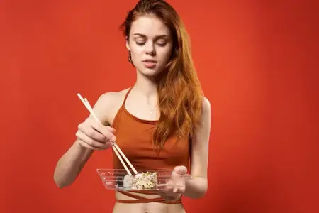 Женщина в красной футболке с палочками для суши, азиатская еда