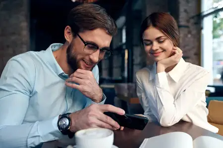 Жизнерадостные мужчина и женщина сидят в кафе за столиком, работают, общаются с помощью технологий