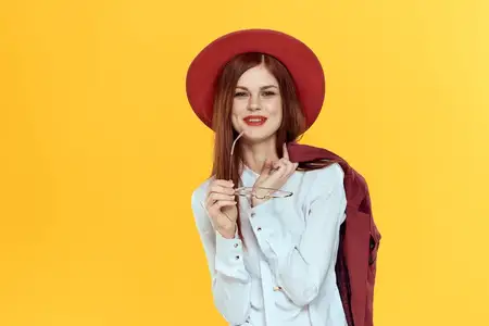 Женщина с пиджаком на плечах, в красной шляпе и белой рубашке, элегантный стиль на жёлтом фоне