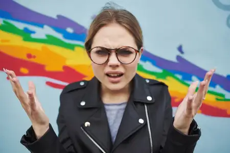Удивленный художник в очках рядом с разноцветным граффити на стене, обрезанный вид