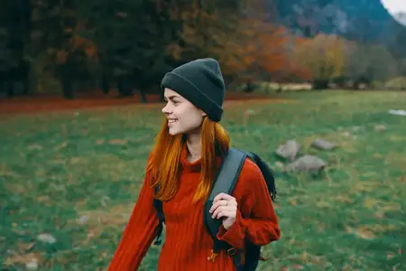 Красивая женщина-туристка с рюкзаком гуляет в парке на природе среди зеленой травы
