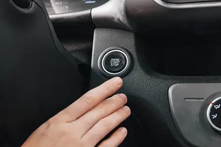 Рука нажимает кнопку запуска и остановки двигателя на рулевом колесе автомобиля, демонстрируя интерьер салона и функции современных технологий, подчеркивая удобство и инновации в автомобильном дизайне