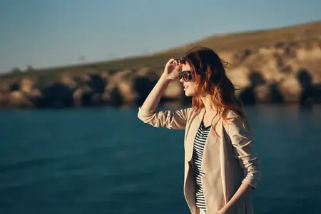 Модель в очках, женщина идет по пляжу у моря, вид сбоку