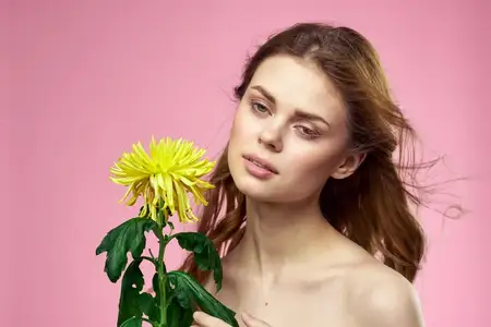 Красивая девушка с жёлтым цветком на розовом фоне, обнажённые плечи, макияж