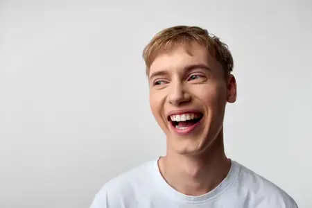 Яркий улыбающийся мужчина в белой футболке, радостное выражение лица и расслабленная поза, чистый фон и дневное освещение, располагающее настроение, идеально подходит для современных визуалов в…
