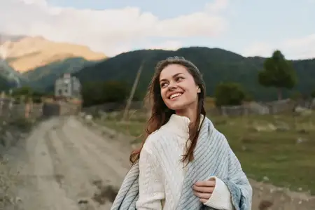 Светящийся портрет на открытом воздухе запечатлел улыбающуюся женщину, укутанную в мягкий шарф и свитер, на фоне живописной долины и далеких холмов