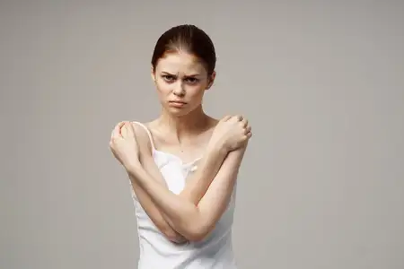 Женщина в белой футболке касается руками своих плеч