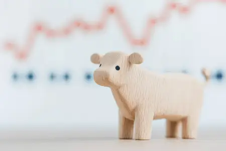 Деревянная фигурка коровы, символизирующая сельское хозяйство, на фоне финансовых графиков, отображающих тенденции роста, что подчеркивает связь между фермерством и экономикой