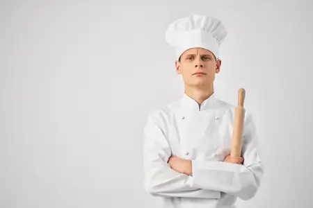 Шеф-повар в белом колпаке на голове занимается приготовлением пищи с использованием кухонной утвари
