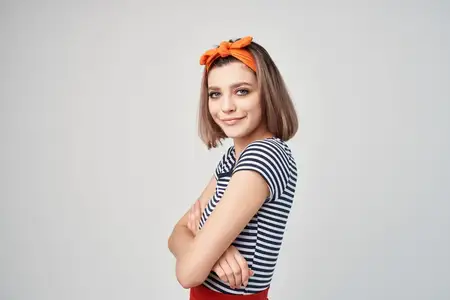 Симпатичная женщина с оранжевой повязкой на голове позирует с модным аксессуаром, выражая эмоции