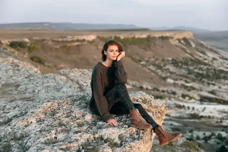 Задумчивая женщина сидит на камне и вдумчиво смотрит на величественный горный пейзаж