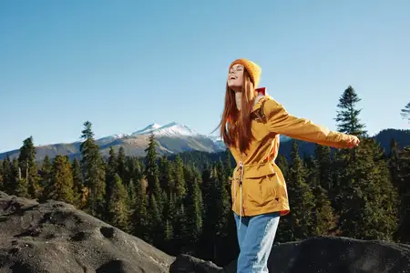 Женщина-туристка в жёлтом дождевике улыбается, показывая зубы, излучая счастье и смех