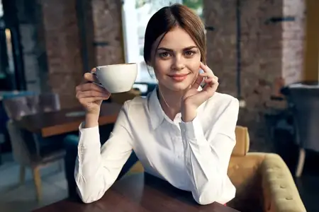 Женщина сидит в кафе за столиком с чашкой напитка