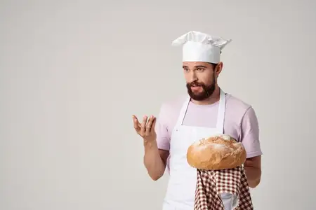 Мужчина в фартуке печёт и готовит свежий хлеб