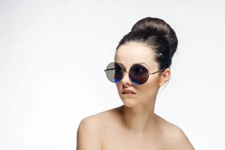 Красивая женщина с обнаженными плечами и в солнечных очках на светлом фоне