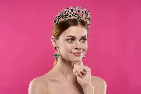 Привлекательная женщина с короной на голове, макияжем и украшениями позирует в студии