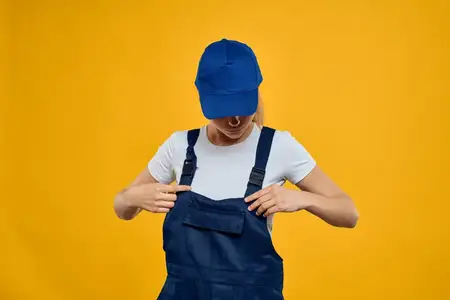 Женщина в рабочей униформе и синей кепке, оказывающая курьерскую службу на жёлтом фоне