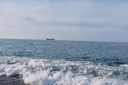 Безмятежный морской пейзаж: открытая вода, накатывающий прибой и далекое судно на горизонте