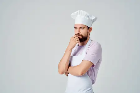 Бородатый шеф-повар мужского пола в белом фартуке на кухне ресторана с кухонной утварью