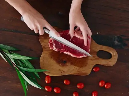 Женщина с ножом в руке нарезает свежее стейковое мясо для жарки на кухне