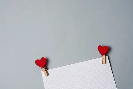 Прищепки в форме сердечек на белом листе бумаги, кадрированный вид, украшение ко Дню святого Валентина