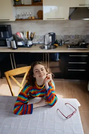 Сцена подчёркивает расслабленное настроение и задумчивое выражение лица, изображая повседневную домашнюю жизнь на современной кухне с тёплым светом и непринуждённой позой