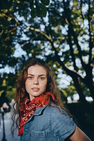 Молодая женщина в стиле современной богемно-вестерн джинсовой уличной моды находится на открытом воздухе в окружении пышной зелени и мягкого солнечного света