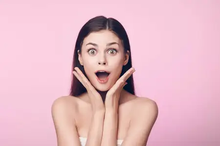Удивлённая молодая женщина с открытым ртом на розовом фоне
