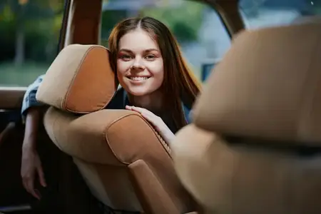 Улыбающаяся молодая женщина с длинными волосами сидит в автомобиле, выражая счастье и приключение