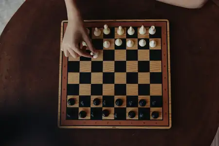 Человек, погружённый в напряжённую стратегическую игру за деревянным столом с классической чёрно-белой шахматной доской