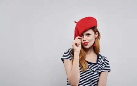 Женщина в полосатой футболке прикасается к красной шляпе на своей голове
