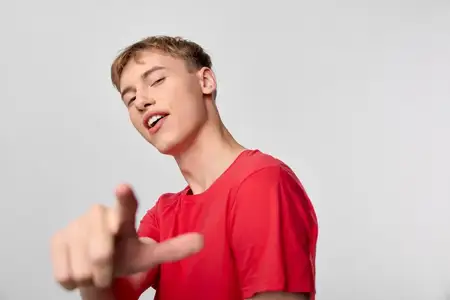 Непринужденная поза с пальцем, указывающим на зрителя, выразительная и энергичная, с молодым человеком в красной рубашке и ярким настроением, идеально подходит для кампаний, учебных пособий или…
