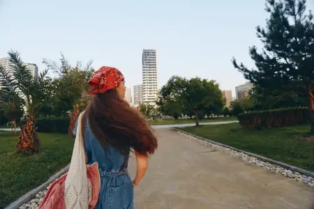 Женщина, ведущая активный образ жизни, одетая в современный бохо-вестерн деним в стиле стрит-стайл, прогуливается по парку среди зеленых деревьев и городских зданий