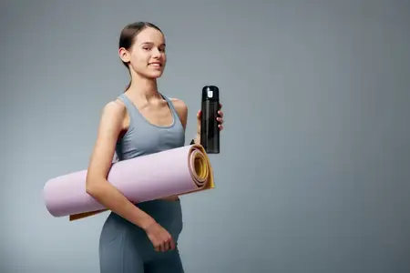 Портрет подтянутой женщины со свернутым ковриком для йоги и бутылкой для воды, демонстрирующий силу, баланс и активный спортивный образ жизни для фитнеса и хорошего самочувствия