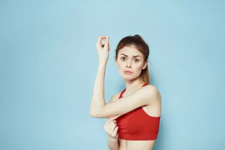 Спортивная женщина в красном топе на лямках тренируется в спортзале на синем фоне