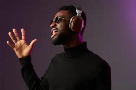 Радостный чернокожий мужчина-модель в наушниках страстно поет, одетый в черную водолазку, освещенный разноцветным фиолетовым фоном, символизируя яркий музыкальный образ жизни