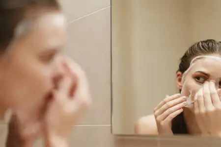 Женщина с энтузиазмом ухаживает за кожей с помощью маски в ванной, что отражает приверженность здоровому образу жизни и расслаблению в окружении нейтральных тонов